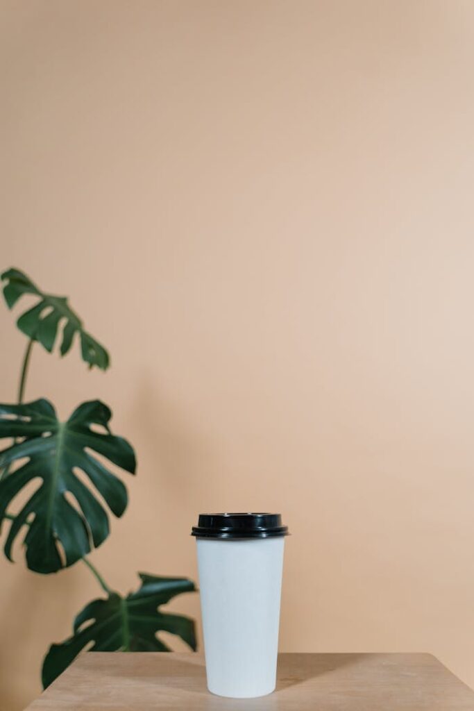 The Art of Drawing Readers In: Your attractive post title goes here A white coffee cup with black lid on a wooden table against a beige background.
